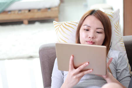 Young woman using tablet at home. A tablet is a wireless touch screen personal computer that is smaller than a notebook but larger than a smartphone.の写真素材