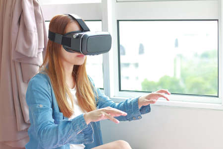 Young woman wearing virtual reality glasses at home. A virtual reality headset is a head-mounted...