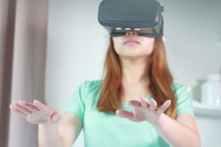Young woman wearing virtual reality glasses at home. A virtual reality headset is a head-mounted device that provides virtual reality for the wearer.の写真素材