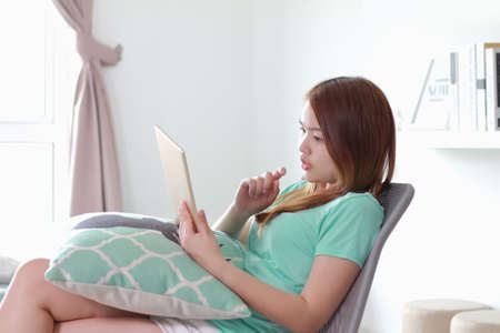 Young woman using tablet at home. A tablet is a wireless touch screen personal computer that is...