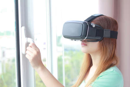 Young woman wearing virtual reality glasses at home. A virtual reality headset is a head-mounted...