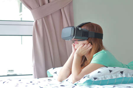 Young woman wearing virtual reality glasses at home. A virtual reality headset is a head-mounted...