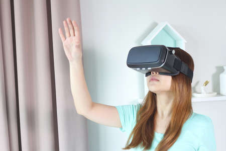Young woman wearing virtual reality glasses at home. A virtual reality headset is a head-mounted...