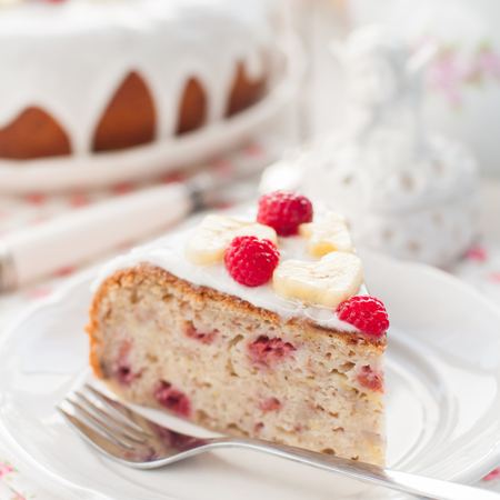 A Piece of Banana Cake with Sugar Glaze Topped with Raspberries and Banana Slices, square, close up, shallow dofの写真素材