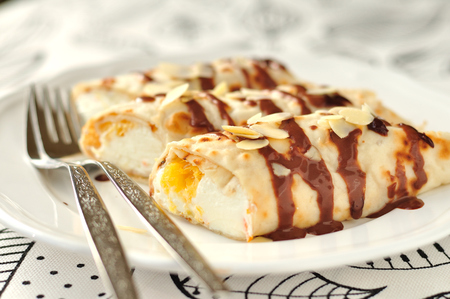 Crepes filled with orange curd cream topped with chocolate sauce and almond flakesの写真素材