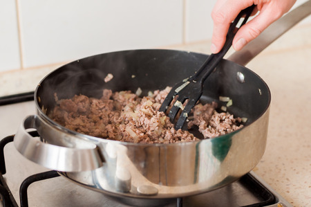 Stirring Minced Beef with Chopped Onions in a Frying Pan on a Gas Stoveの写真素材