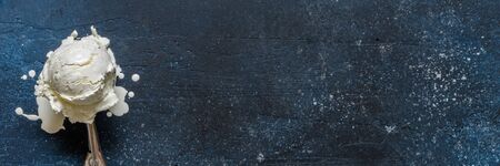 Melting Vanilla Ice Cream Ball in a Stainless Steel Scoop Spoon on Blueの写真素材