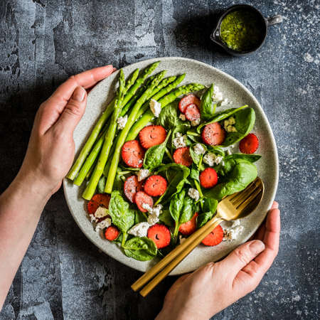Hands Holding a Plate of Strawberry, Spinach, Asparagus and Feta Salad with Pesto Dressingの写真素材