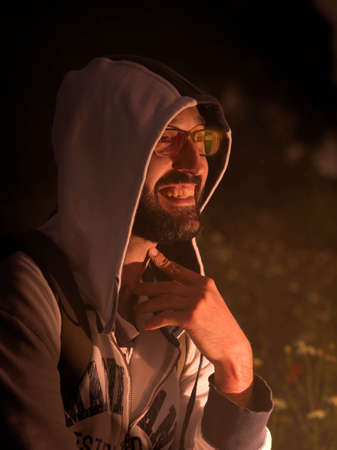 Young man with hood smiling around a campfire.の写真素材