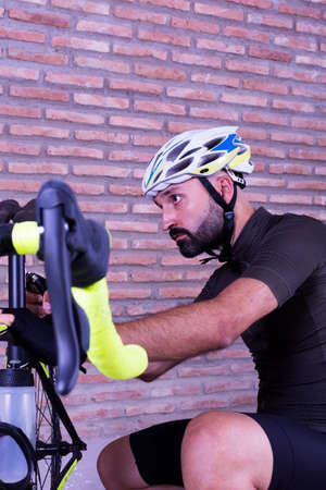 Cyclist adjusting his bike next to a brick wall