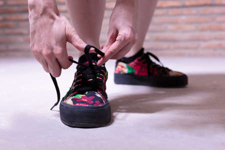 Young woman standing tying her colourful canvas shoes