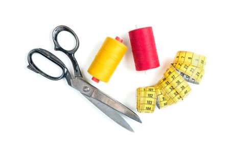 Sewing thread coil with old metal scissors and yellow measuring tape on white background