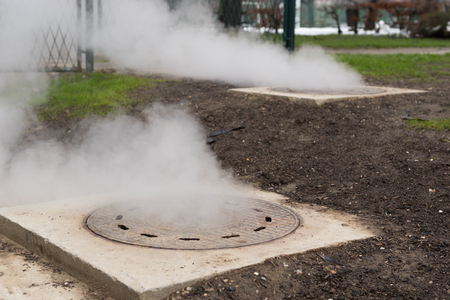 Hot white steam coming out of metal manhole or metal hatchの写真素材