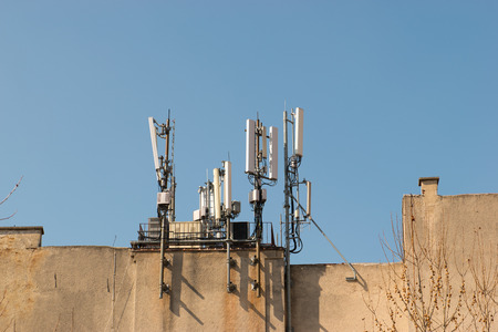 Mobile antenna on the roof of a building against blue sky. Broadcasting and network communicators,...