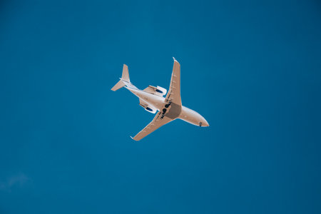 White private jet in the sky, bottom view. Airplane landing. Airplane on blue isolated background.