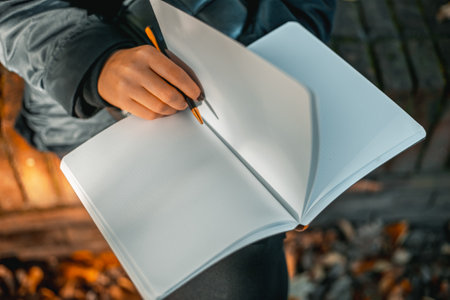 Young woman writing in a diary in an autumn park. Closeup image of a woman writing on a blank notebook. Woman working outdoors.の写真素材