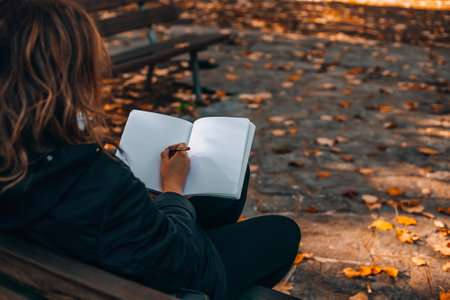Woman writing in a diary in an autumn park. Closeup image of a woman writing on a blank notebook.の写真素材