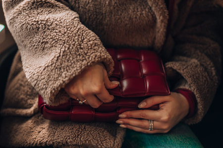 Milan, Italy - December, 17, 2023 Woman wears leather red mini Bottega Veneta Cassette bag, street style details. Woman on a train at Milan Central Stationのeditorial素材