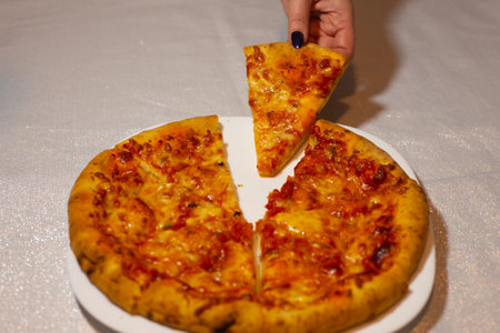 Womans hand takes a slice of pizza. Original Italian pizza Margherita with cheese and tomato sauce on a white plateの写真素材