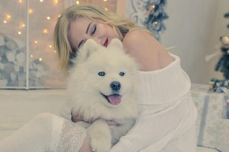 beautiful blonde in white clothes with a white husky on the background of the fireplaceの写真素材