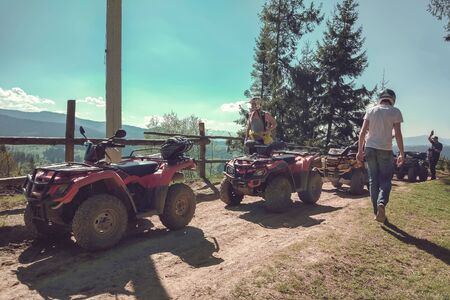 A string of Quad bike on a rural road on the background of mountains and fir trees, people made a...