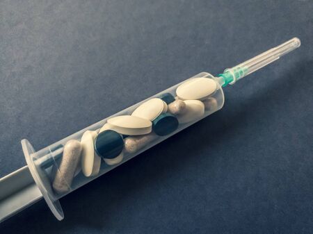 The treatment of the disease. Close-up of a syringe with a variety of tablets and capsules inside. Gray backgroundの写真素材