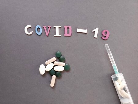 Coronavirus outbreak. Coronavirus 2019 disease, COVID 19, nCoV concept on gray background. A lot of different pills and a syringe filled with pills. Text COVID-19 in colorful lettersの写真素材