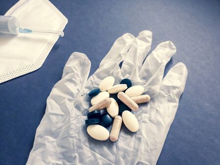 the concept of medical care. A handful of pills in a disposable rubber glove on the background bandage and syringe, the fight against the pandemic coronavirusの写真素材