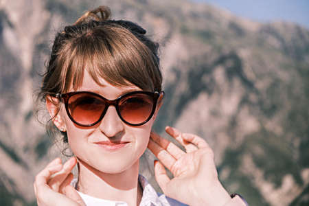 Portrait confident girl looks into the camera wearing sunglasses against the background of nature on a sunny dayの写真素材