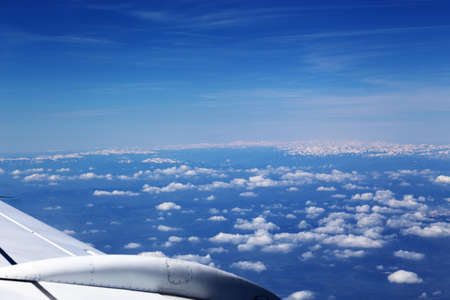 Wing of the plane on blue sky background and snowy mountains below, view from window of a jet plane wing with beautiful weatherの写真素材