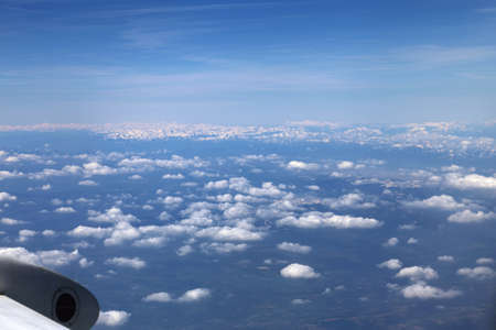 Wing of the plane on blue sky background and snowy mountains below, view from window of a jet plane wing with beautiful weatherの写真素材