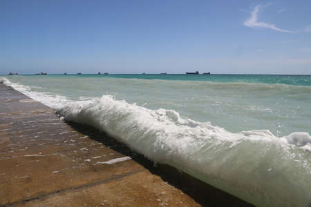 Pier on the sea with the waves and the ships on the horizon の写真素材