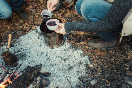 A group of people drinking tea, coffee and mulled wine in the outdoor.Mulled wine, tea and coffee cooked over a campfire on the nature.の写真素材