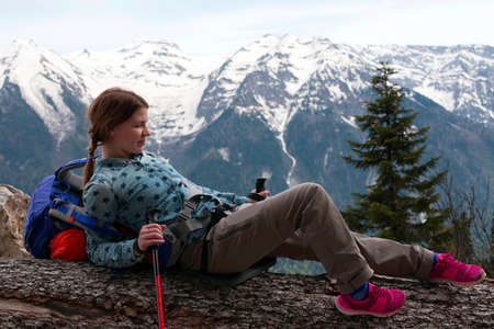 Young positive woman hiking with trekking poles and backpack resting. Travel Lifestyle concept Summer journey vacations outdoor mountains on background. Happy girl.の写真素材