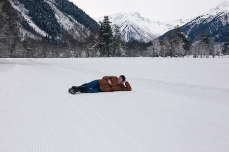 Man positive rejoices lying in the snow against the backdrop of mountain scenery.
Lifestyle adventure. The concept of travel, health and well-being.の写真素材
