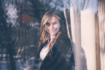 View through the window of a successful woman using a mobile phone while relaxing in a cafe. Concept of business young girl calling from mobile phone.の写真素材