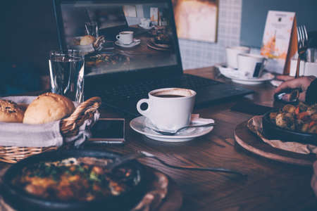 A cup of coffee and breakfast, a laptop computer in a modern cafe bar, a picture of a freelancer. Cozy atmosphere of the designer.の写真素材