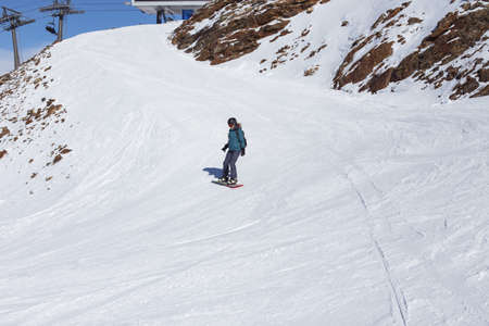 A snowboarder girl is riding on a background of mountains in the winter season. Sports type of vacation. The concept of snowboarding, success, lifestyle, adventure, travel.の写真素材