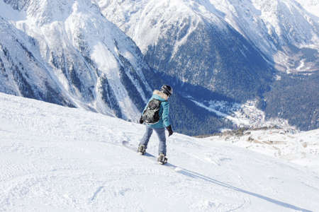 A snowboarder girl is riding on a background of mountains in the winter season. Sports type of vacation. The concept of snowboarding, success, lifestyle, adventure, travel.の写真素材
