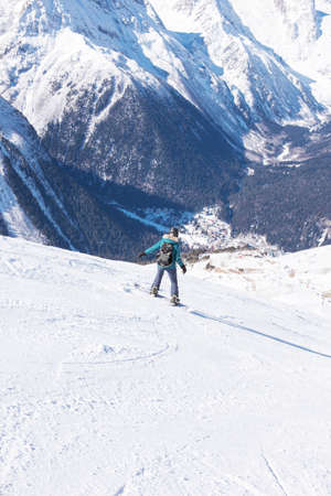 A snowboarder girl is riding on a background of mountains in the winter season. Sports type of vacation. The concept of snowboarding, success, lifestyle, adventure, travel.の写真素材