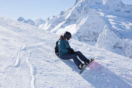 A snowboarder girl in the mountains enjoys nature in the winter season. Sports type of vacation. The concept of snowboarding, success, lifestyle, adventure, travel.の写真素材
