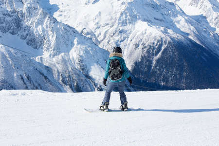 A snowboarder girl is riding on a background of mountains in the winter season. Sports type of vacation. The concept of snowboarding, success, lifestyle, adventure, travel.の写真素材