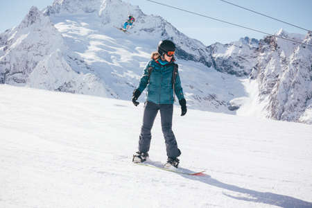 A snowboarder girl is riding on a background of mountains in the winter season. Sports type of vacation. The concept of snowboarding, success, lifestyle, adventure, travel.の写真素材