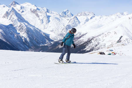 A snowboarder girl is riding on a background of mountains in the winter season. Sports type of vacation. The concept of snowboarding, success, lifestyle, adventure, travel.の写真素材