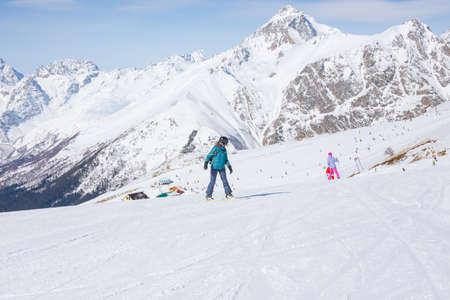A snowboarder girl is riding on a background of mountains in the winter season. Sports type of vacation. The concept of snowboarding, success, lifestyle, adventure, travel.の写真素材