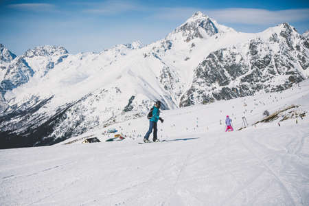A snowboarder girl is riding on a background of mountains in the winter season. Sports type of vacation. The concept of snowboarding, success, lifestyle, adventure, travel.の写真素材