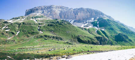 Mountain landscape in summer, quiet idyllic scene of green glades, peaks and snowy slopes. Lifestyle tourism and travel, adventure. Alpine rocky view of the meadow and the lake.の写真素材