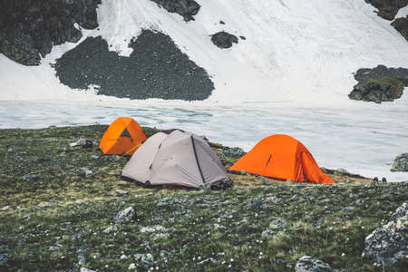 Camping tents in high mountains against the backdrop of rocky peaks and a frozen lake. The concept...