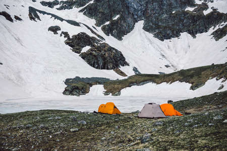 Camping tents in high mountains against the backdrop of rocky peaks and a frozen lake. The concept of a sports lifestyle adventure vacation outdoor. Landscape shooting camping equipment.の写真素材