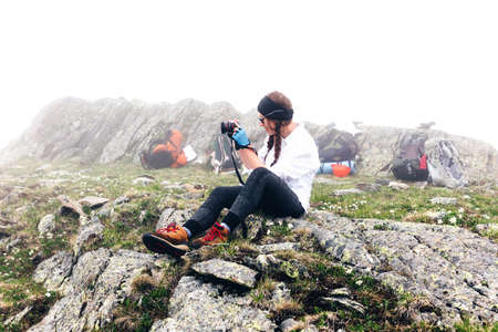 A girl travels in the mountains taking pictures with a camera, camping backpack background. The concept of adventure, lifestyle hikes.の写真素材